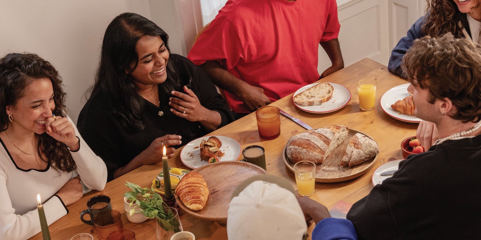 Friends laughing around a table with bread, pastries, and drinks